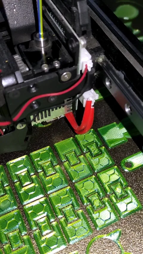 Close-up video of a 3D printer nozzle creating colorful green plastic objects Stock Footage 311157348