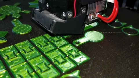 Close-up video of a 3D printer nozzle creating colorful green plastic objects Stock Footage 311157687