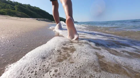 Close-up video of bare feet walking along the sandy beach shoreline as gentle Stock Footage 313810662