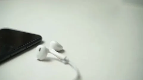 Close up video of black smartphone with plugged in white earphones on white tabl Video stock 163863140