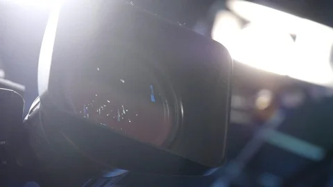 Close-up of a video camera lens with bright production lights on set. Vidéo 97149105