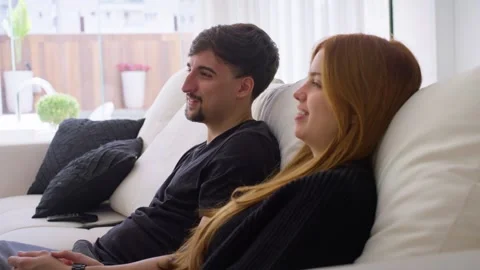 Close up video of a couple sitting on the couch talking while watching tv. Video stock 247660821