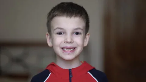 Close-up video of cute young boy showing teeth at camera in red hoodie. Stock Footage 337184884