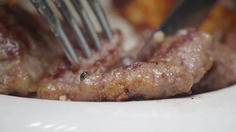 Close up video of fork and knife cutting into grilled meat on white plate. 库存影片 331719613