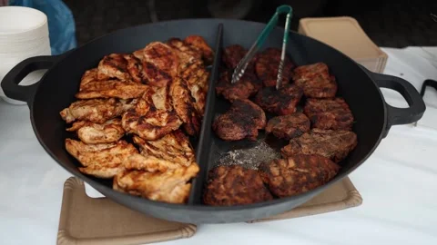 A close-up video of grilled meat on a large pan. The left side shows grilled chi Stock Footage 303286385
