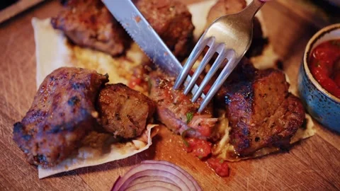 Close up video of hands with fork and knife cutting piece of grilled meat, .. Stock Footage 339764726