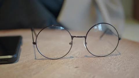 Close up video of hands picking up round spectacles from wooden table next .. Stock Footage 331985358