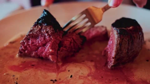 Close up video of hands using fork and knife to cut tender steak on plate w.. Vídeos de archivo 339791582