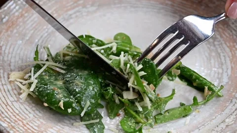 Close up video of hands using a knife and fork to cut a fresh spinach and r.. Vídeos de archivo 339641121