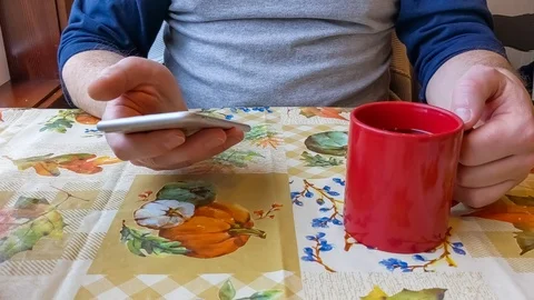 Close up video of a man drinking coffee while scrolling on his cell phone 動画素材 124881812