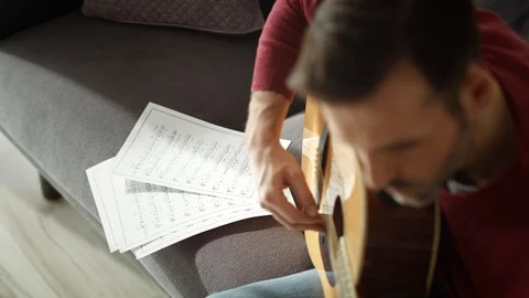 Close up video of man practicing guitar play on sofa.  Stock-Footage 128853304