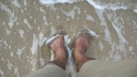 A Close up video of a Ocean Waves flowing over the man's feet Stock Footage 166684404