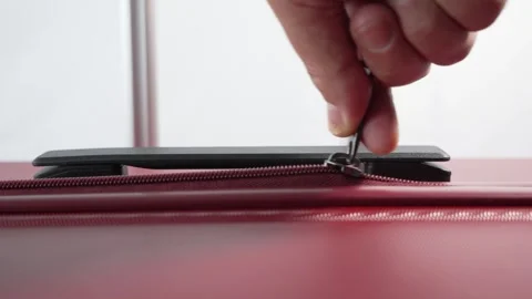 A close-up video shows a hand pulling a single zipper on a red suitcase. Stock Footage 317083670