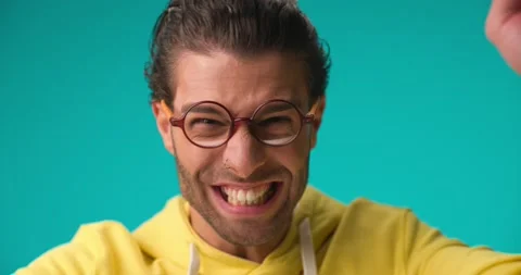 Close up video of surprised young man in yellow hoodie with glasses celebrating Stock Footage 230127848