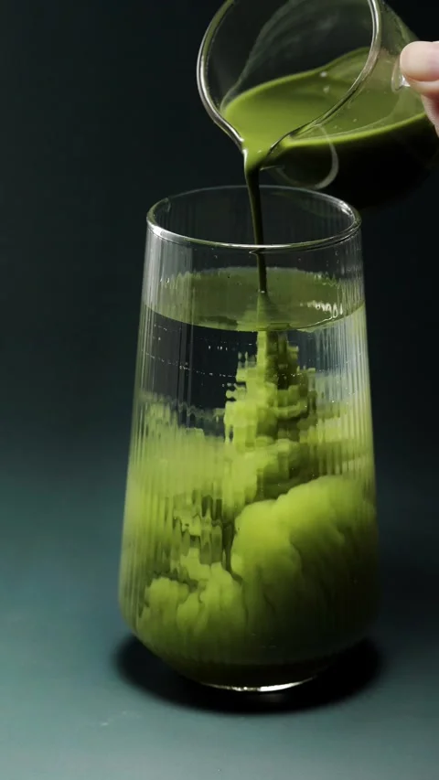 Close-up video of vibrant green matcha mixing with clear water inside a rib.. Видео 345125482