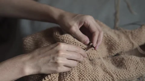 Close-up video of woman's hands knitting a beige jumper before grey background Stock Footage 282976115