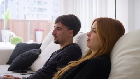 Close-up video Young couple in black clothes watching TV on the living room sofa Stock Footage 247660657