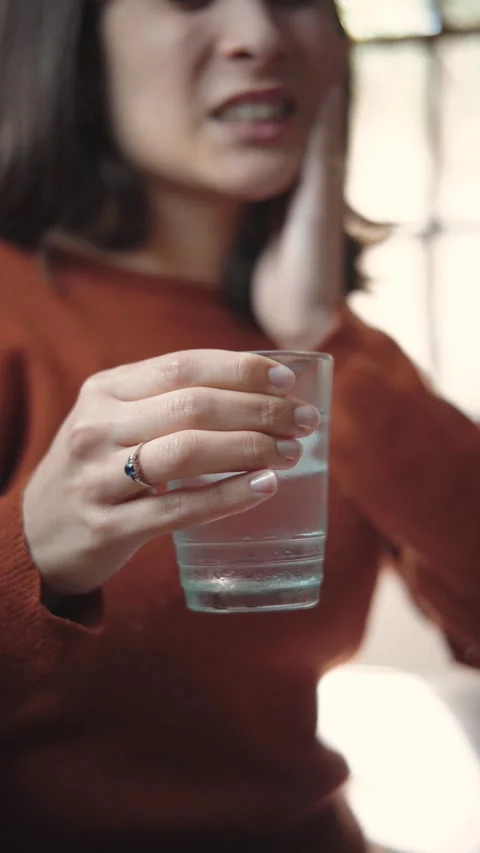 Close-up video of a young woman’s hand holding a glass of ice water to soothe se Stock Footage 346327128