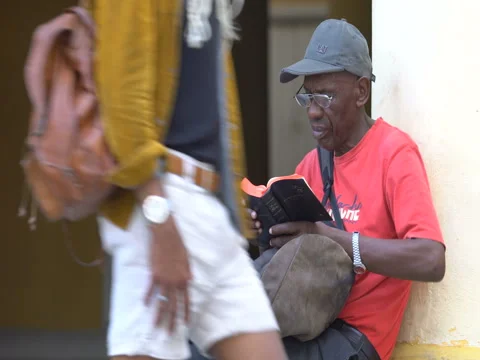 Close-up view Afro-American man dressed red t-shirt, hat, glasses sits at the Stock Footage 69559172