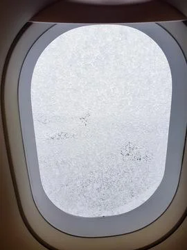 Close-up view of an airplane window covered with frost and ice crystals while th 스톡 사진