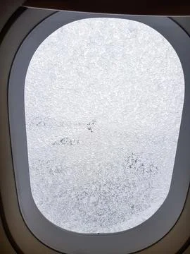 Close-up view of an airplane window covered with frost and ice crystals while th Фото