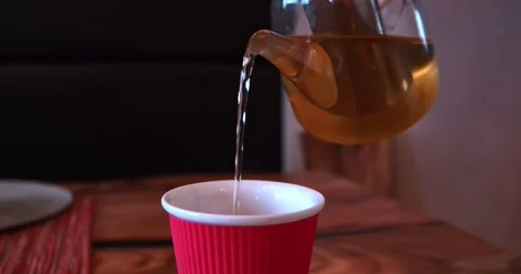 Close view of amber tea flowing from glass pot into bright red cup on table Stock Footage 340333542