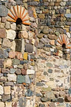 Close-up view of ancient stone wall with small arched openings and colorful.. Stock Photos