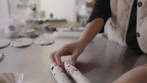 Close up view of baker hands skillfully rolling log of fresh raisin dough on Stock Footage 328983647