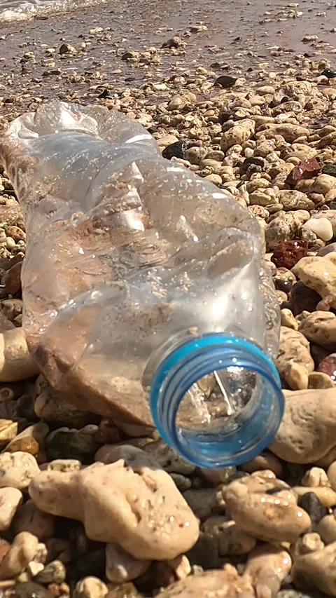 A close-up view of a beach scene, highlighting a plastic bottle partially buried Stock Footage 331806873