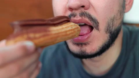 Close up view of bearded man biting a sweet chocolate eclair Stock Footage 204998007
