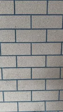 Close-up view of a beige brick wall with dark grout lines, textured surface. Stock Photos