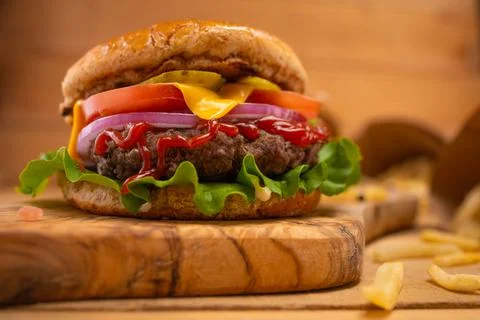 Close-up view of big appetizing burger with bacon wooden board against beige  Stock Photos
