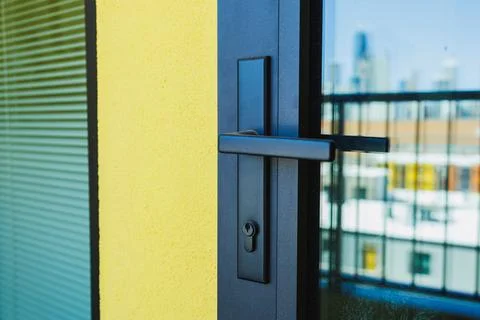 Close-up view of a black door handle on a yellow wall with city buildings i.. Photos