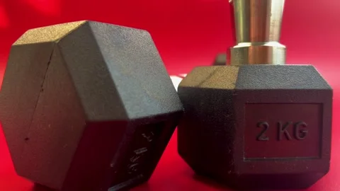 Close-up view of black hexagonal dumbbells on a vibrant red background Stock Footage 321739783