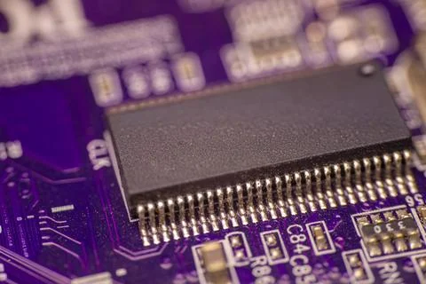 Close-up view of a black microchip mounted on a purple printed circuit boar.. Stock Photos