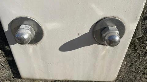 Close-up view of bolts securing a white metal plate to a textured stone wal.. 库存照片