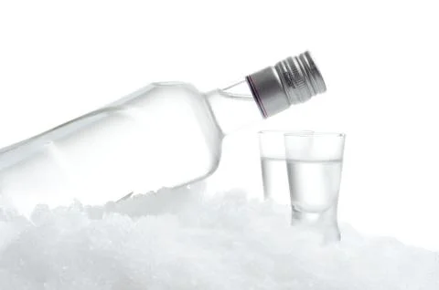 Close-up view of bottle lying on ice with two glasses of vodka on white backg Stock Photos