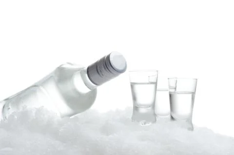 Close-up view of bottle lying on ice with three glasses of vodka on white bac Stock Photos