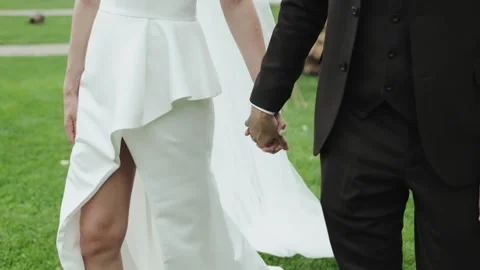 Close-up view . A bride and groom stroll hand in hand in a lush green field Stock Footage 322051130