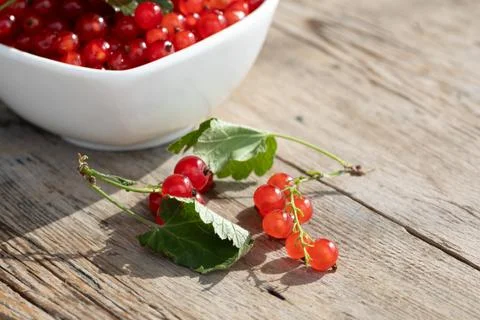 Close view of bright red currants spilling from white bowl onto weathered Stock Photos