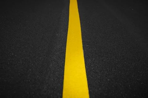 A close-up view of a bright yellow dividing line on a dark asphalt road surfa Fotos Stock