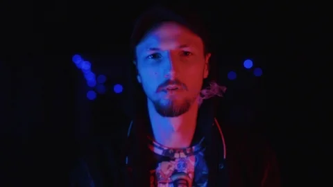 Close up view of brutal stylish young man smoking cigarette under neon lights in Stock Footage 111221133