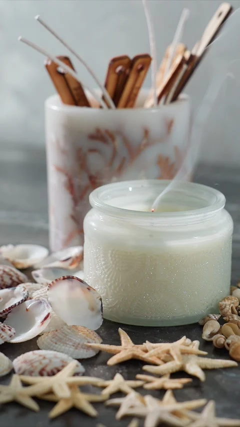 Close up view of burning candle in frosted glass surrounded by seashells and Video stock 344671340