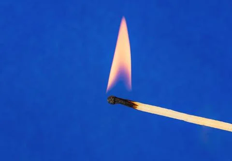 Close-up view of burning match with flame on blue blurred background. Stock Photos