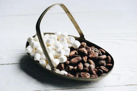 Close up view of cacao beans and sweet marshmallow in metal bowl on wooden ta Stock Photos