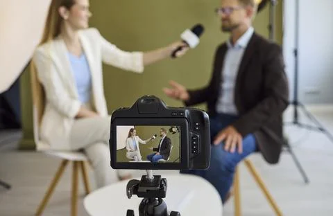 Close view of camera recording journalist interviewing guest in modern studio Stock Photos