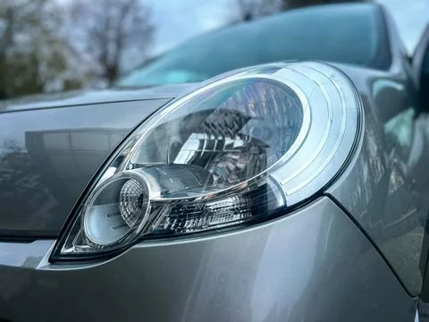 Close view of a car headlight in a parking area during the day with trees a.. Stock Photos
