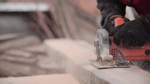 Close-up view of carpenter in work gloves sawing board with help of modern Stock Footage 132325174