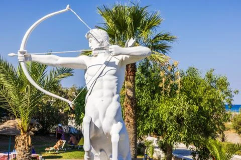 Close-up view of centaur archer statue with bow among palm trees at resort. Stock Photos