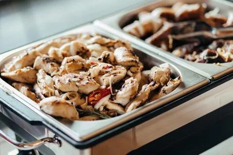 A close-up view of a chafing dish with two white serving trays filled with Stock Photos